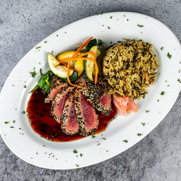 Seared tuna with sesame crust, wild rice, grilled zucchini, and carrots on a white plate.