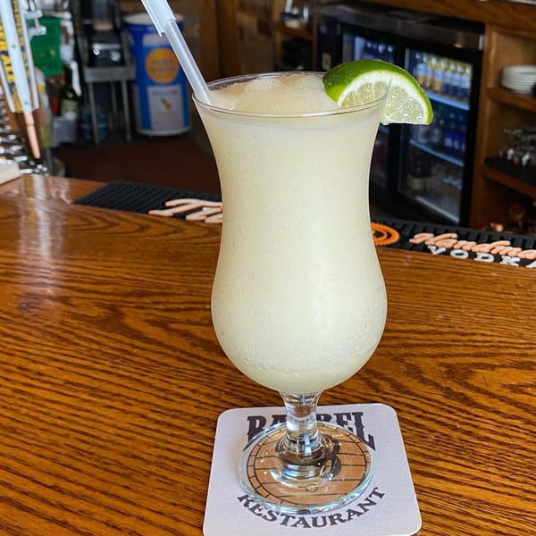 A Barrel 28 frozen margarita with a lime wedge and straw on a branded coaster at the bar.