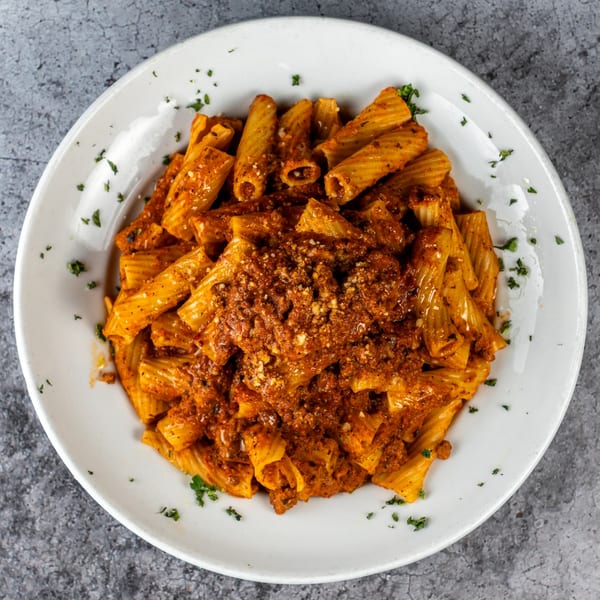 Rigatoni pasta with a rich red sauce, sprinkled with cheese and parsley, in a white bowl.