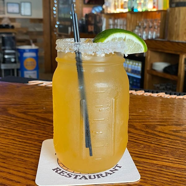 A Barrel 28 margarita in a mason jar with a salted rim and lime wedge on a wooden bar.