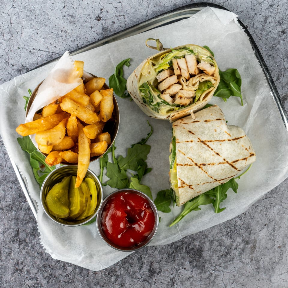 Chicken Caesar wrap with fries, pickles, and ketchup on a tray with parchment paper.