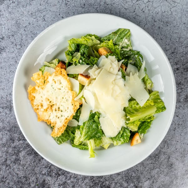 Caesar salad with romaine lettuce, croutons, shaved Parmesan, and a large cheese crisp.