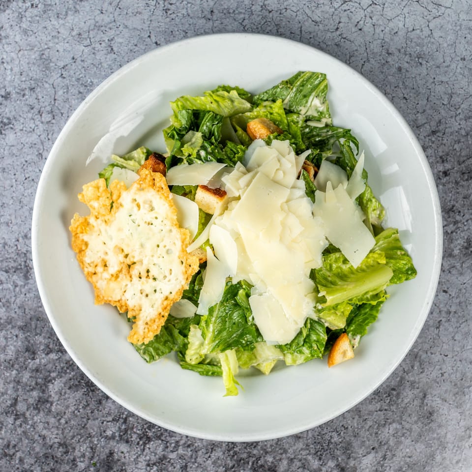 Caesar salad with romaine lettuce, croutons, shaved Parmesan, and a large cheese crisp.