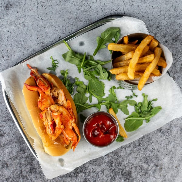 Barrel 28's lobster roll with fries, ketchup, and arugula on a metal tray.